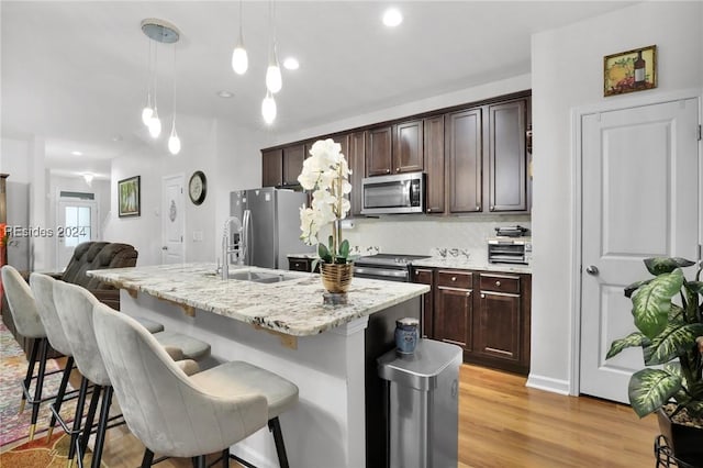 kitchen featuring dark brown cabinetry, a breakfast bar area, hanging light fixtures, a center island with sink, and stainless steel appliances