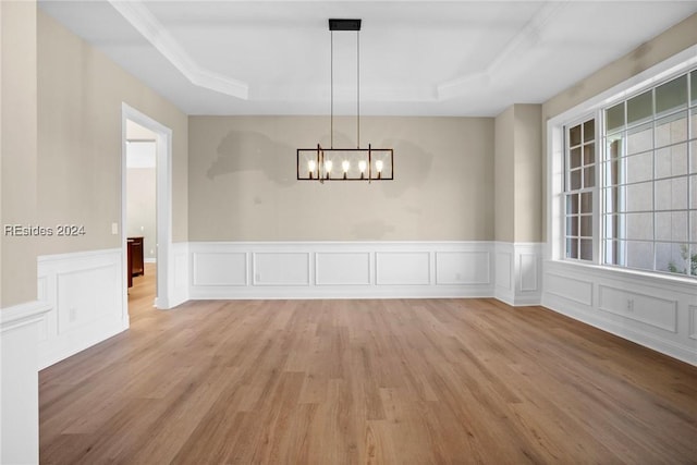 unfurnished dining area with a raised ceiling, a notable chandelier, and light hardwood / wood-style flooring