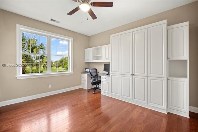 unfurnished office with ceiling fan, built in desk, and hardwood / wood-style floors