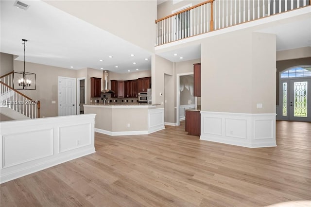 unfurnished living room with a high ceiling, a notable chandelier, and light wood-type flooring