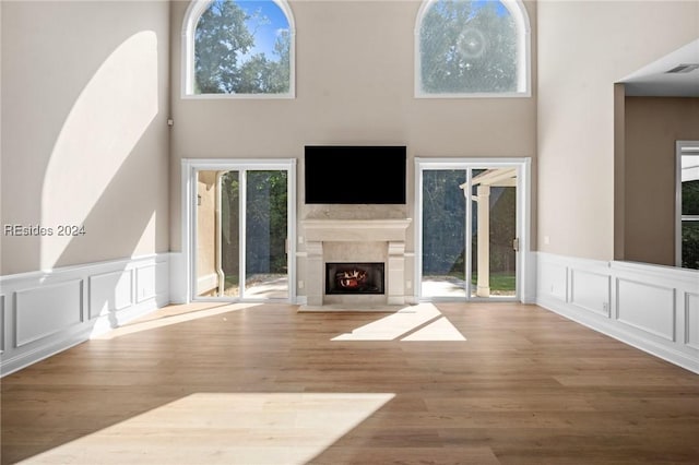 unfurnished living room with a towering ceiling, a premium fireplace, and hardwood / wood-style floors