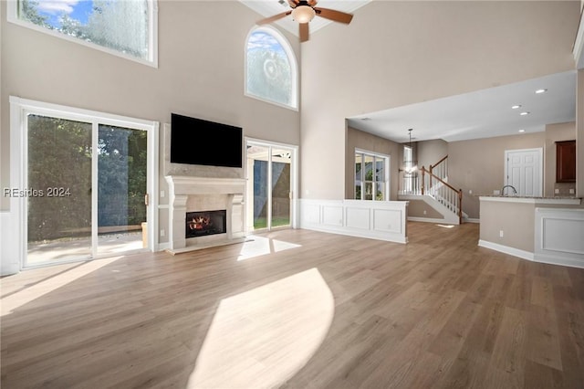 unfurnished living room with a premium fireplace, a towering ceiling, a healthy amount of sunlight, and light hardwood / wood-style flooring