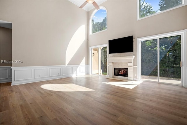 unfurnished living room with wood-type flooring, a premium fireplace, ceiling fan, and a high ceiling