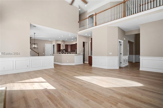 unfurnished living room featuring a towering ceiling, ceiling fan with notable chandelier, and light wood-type flooring