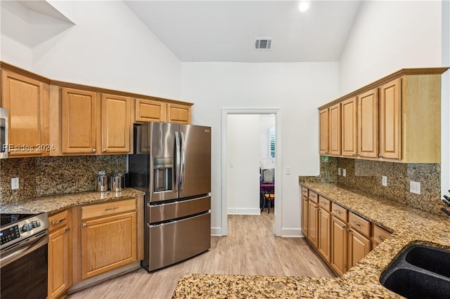 kitchen with light stone countertops, light hardwood / wood-style flooring, stainless steel appliances, and high vaulted ceiling