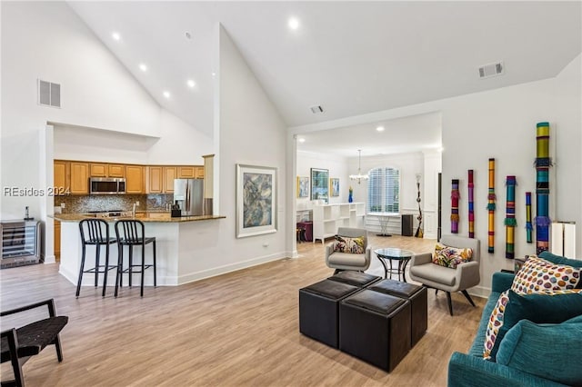 living room with an inviting chandelier, light hardwood / wood-style floors, and high vaulted ceiling