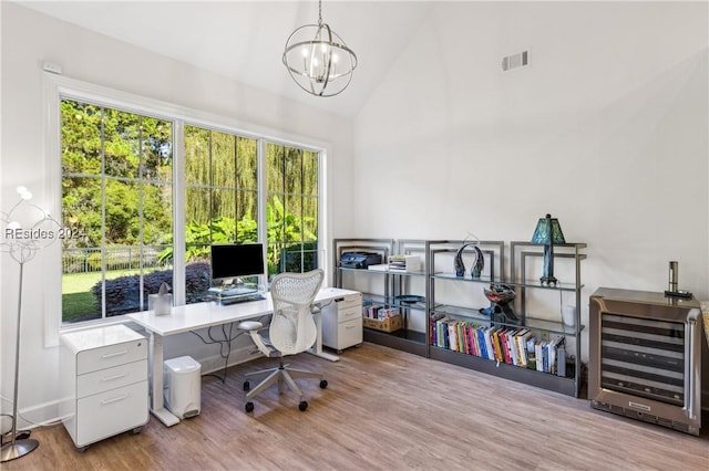 home office with high vaulted ceiling, heating unit, an inviting chandelier, and light hardwood / wood-style flooring