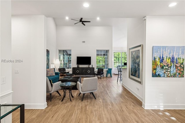 living room featuring a towering ceiling, ceiling fan, and light hardwood / wood-style flooring