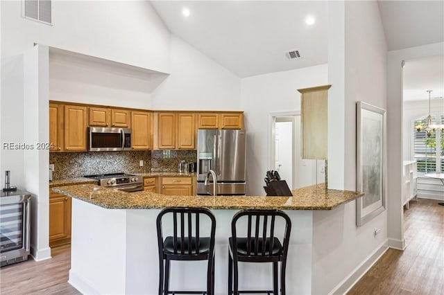 kitchen featuring appliances with stainless steel finishes, kitchen peninsula, high vaulted ceiling, and stone countertops