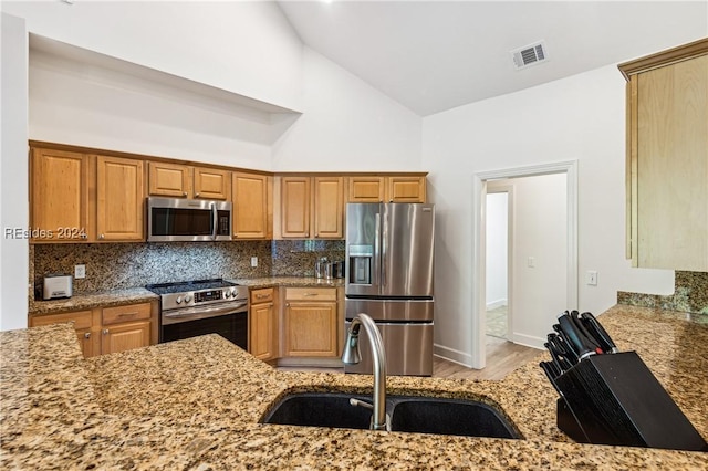 kitchen featuring sink, high vaulted ceiling, stainless steel appliances, light stone countertops, and decorative backsplash