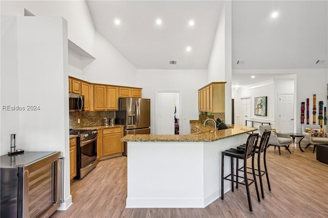 kitchen featuring appliances with stainless steel finishes, high vaulted ceiling, a breakfast bar area, beverage cooler, and kitchen peninsula