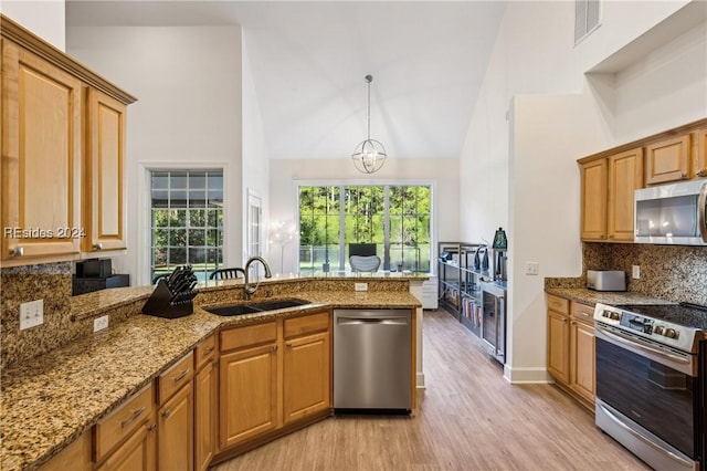 kitchen with sink, decorative light fixtures, stainless steel appliances, and high vaulted ceiling