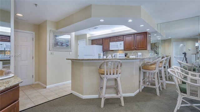 kitchen with a kitchen bar, light stone counters, light tile patterned floors, kitchen peninsula, and white appliances