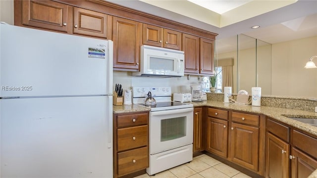 kitchen with sink, hanging light fixtures, light tile patterned floors, white appliances, and light stone countertops