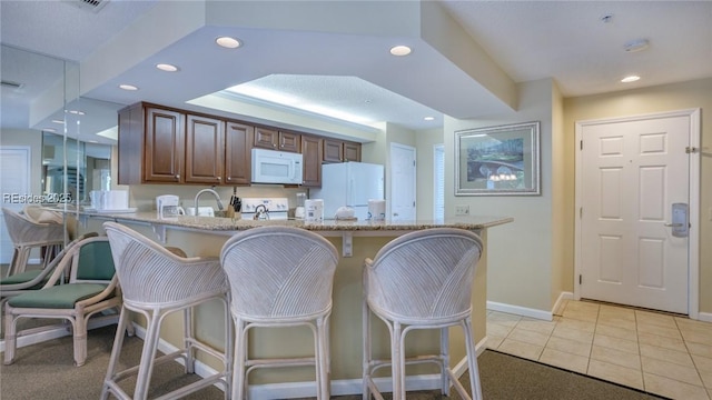 kitchen featuring white appliances, a kitchen breakfast bar, light stone counters, light tile patterned flooring, and kitchen peninsula