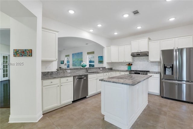 kitchen with light stone counters, stainless steel appliances, kitchen peninsula, and white cabinets