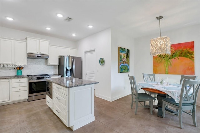 kitchen featuring stainless steel appliances, white cabinetry, pendant lighting, and dark stone countertops