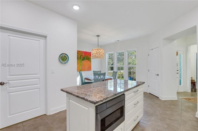 kitchen featuring pendant lighting, stainless steel microwave, white cabinetry, a center island, and light stone countertops