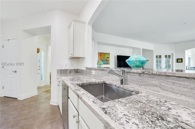 kitchen with sink, white cabinetry, light stone counters, light tile patterned floors, and stainless steel dishwasher