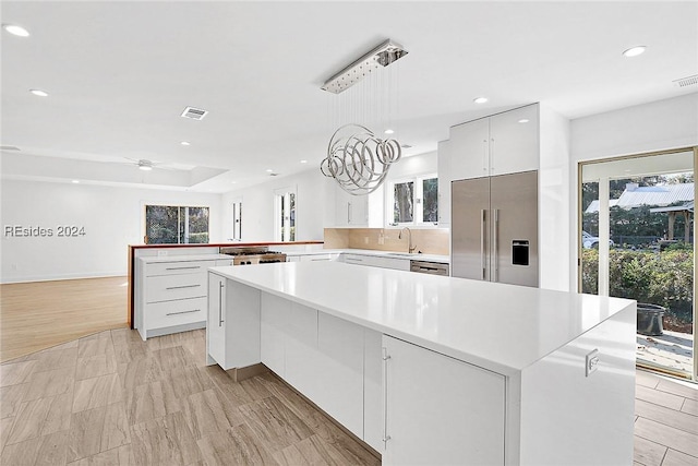 kitchen featuring decorative light fixtures, a center island, white cabinets, and built in refrigerator