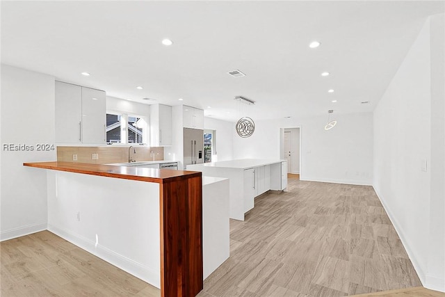 kitchen with sink, backsplash, stainless steel built in refrigerator, white cabinets, and kitchen peninsula