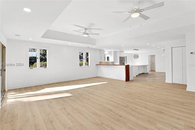 unfurnished living room with a raised ceiling, ceiling fan, and light hardwood / wood-style flooring