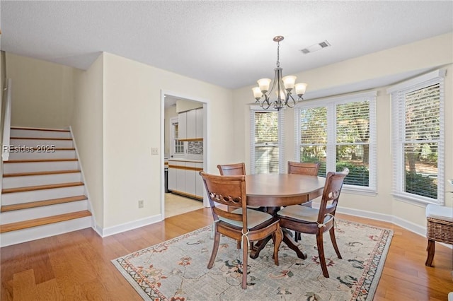 dining room with a chandelier, a textured ceiling, and light wood-type flooring