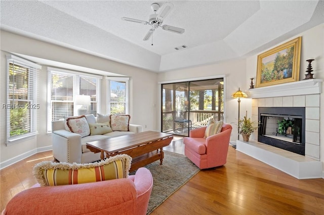 living room featuring a textured ceiling, light hardwood / wood-style flooring, a raised ceiling, ceiling fan, and a fireplace