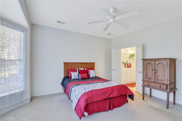 bedroom featuring light colored carpet, a textured ceiling, ceiling fan, and ensuite bath