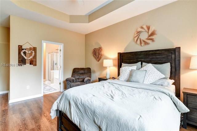 bedroom with a raised ceiling, ensuite bathroom, hardwood / wood-style floors, and ceiling fan