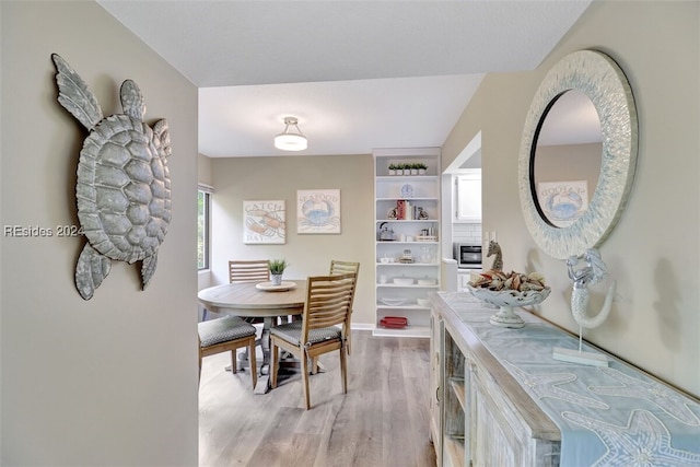 dining room with built in shelves and light hardwood / wood-style flooring