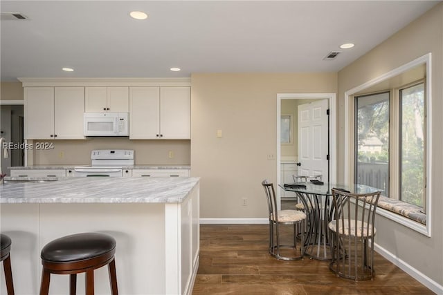 kitchen featuring a breakfast bar, white cabinetry, light stone countertops, dark wood-type flooring, and white appliances