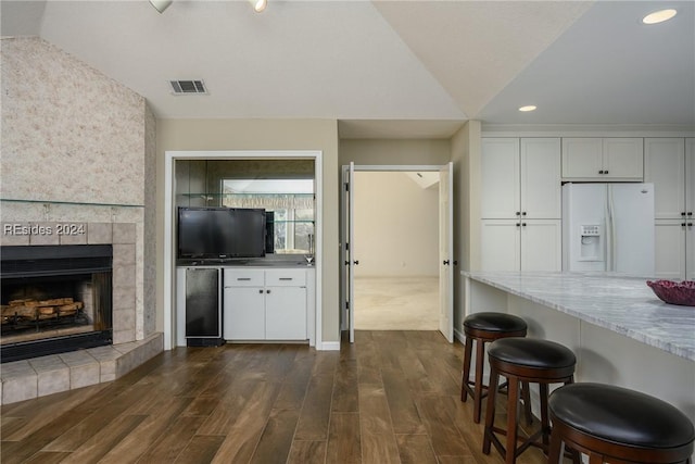 kitchen featuring a fireplace, white cabinetry, dark hardwood / wood-style flooring, white refrigerator with ice dispenser, and light stone countertops