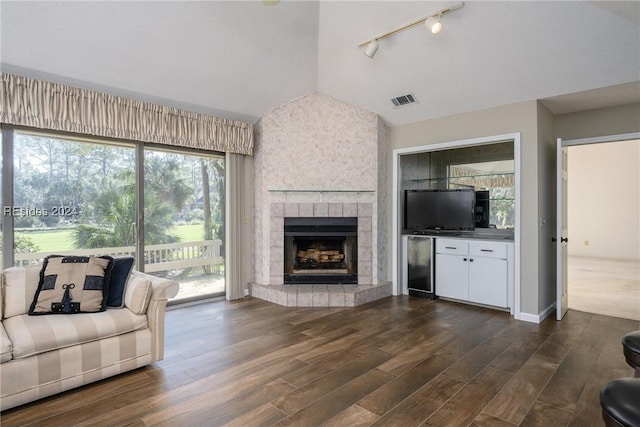 living room featuring a tiled fireplace, lofted ceiling, and dark wood-type flooring