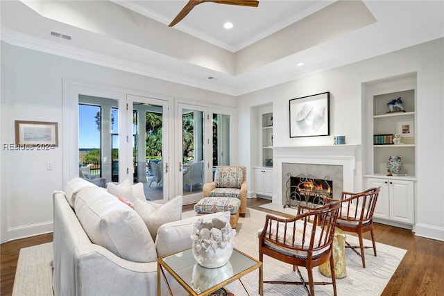 living room featuring crown molding, a tray ceiling, dark wood-type flooring, and built in shelves