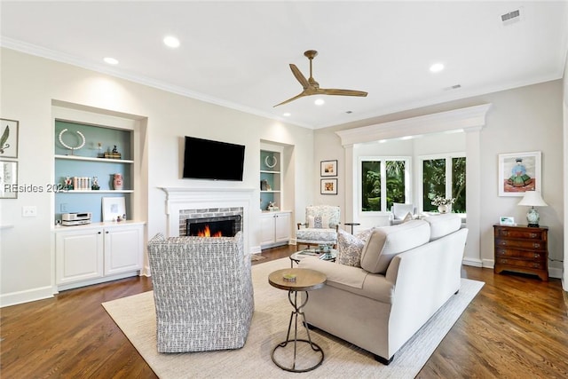 living room featuring built in shelves, a fireplace, dark wood-type flooring, and crown molding