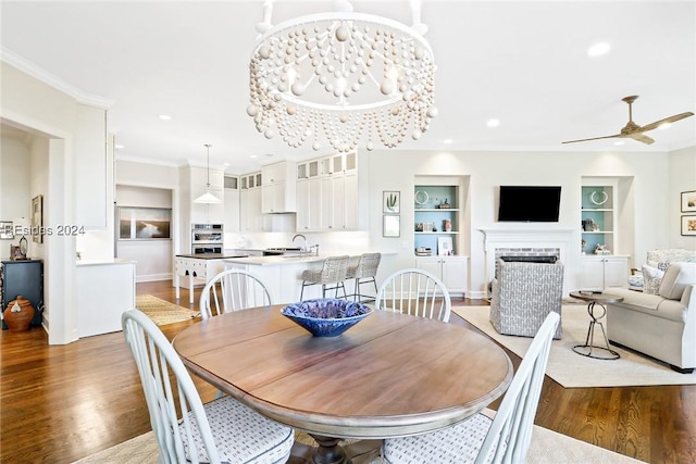 dining room with ceiling fan with notable chandelier, sink, hardwood / wood-style flooring, crown molding, and built in shelves