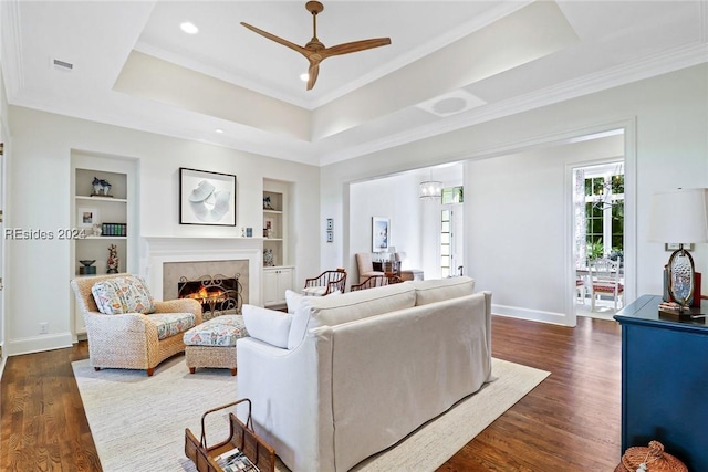 living room featuring dark wood-type flooring, ornamental molding, a raised ceiling, and built in features