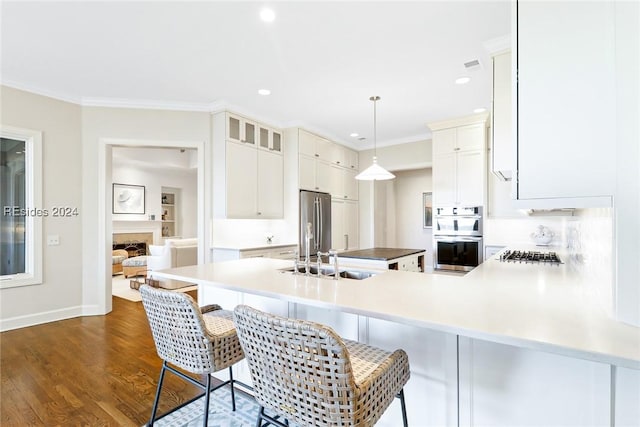 kitchen with appliances with stainless steel finishes, decorative light fixtures, a breakfast bar area, white cabinets, and kitchen peninsula