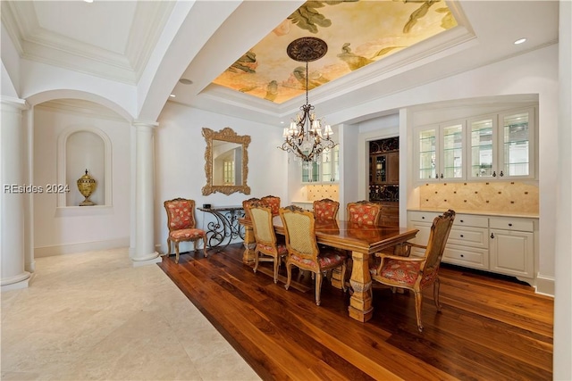 dining space featuring an inviting chandelier, crown molding, hardwood / wood-style flooring, and ornate columns