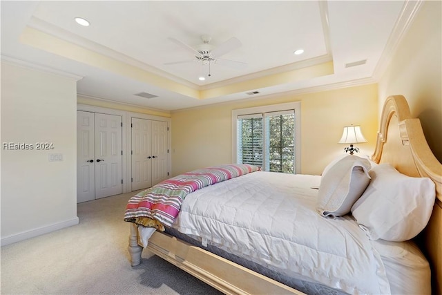 carpeted bedroom featuring multiple closets, ceiling fan, ornamental molding, and a raised ceiling