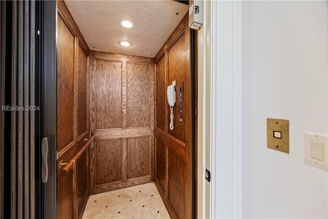 interior details with a textured ceiling, wooden walls, and elevator