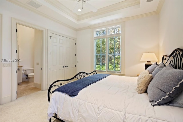 carpeted bedroom with ceiling fan, a raised ceiling, a closet, and ensuite bath