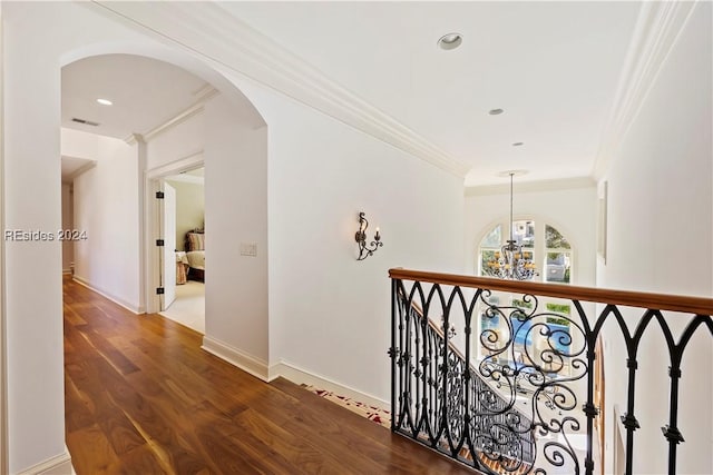 corridor with crown molding, wood-type flooring, and an inviting chandelier