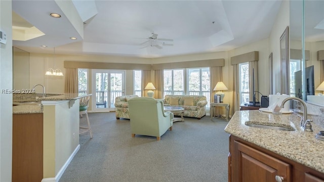 carpeted living room with ceiling fan, a tray ceiling, and sink