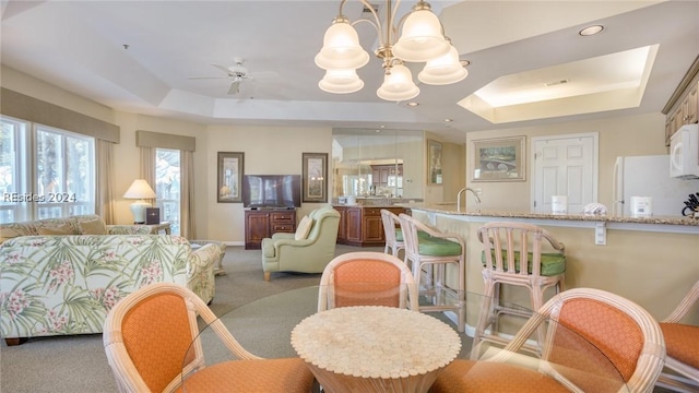 dining area featuring sink, a tray ceiling, ceiling fan with notable chandelier, and carpet