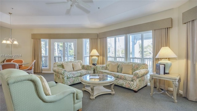 carpeted living room with ceiling fan with notable chandelier and a tray ceiling