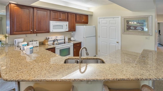 kitchen with sink, a breakfast bar area, kitchen peninsula, light stone countertops, and white appliances