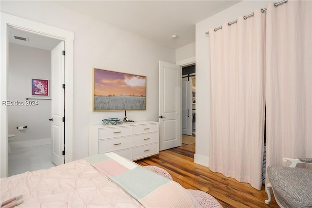 bedroom with ensuite bathroom, a barn door, and light hardwood / wood-style floors