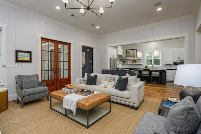 living room featuring french doors, ornamental molding, light wood-type flooring, and a notable chandelier